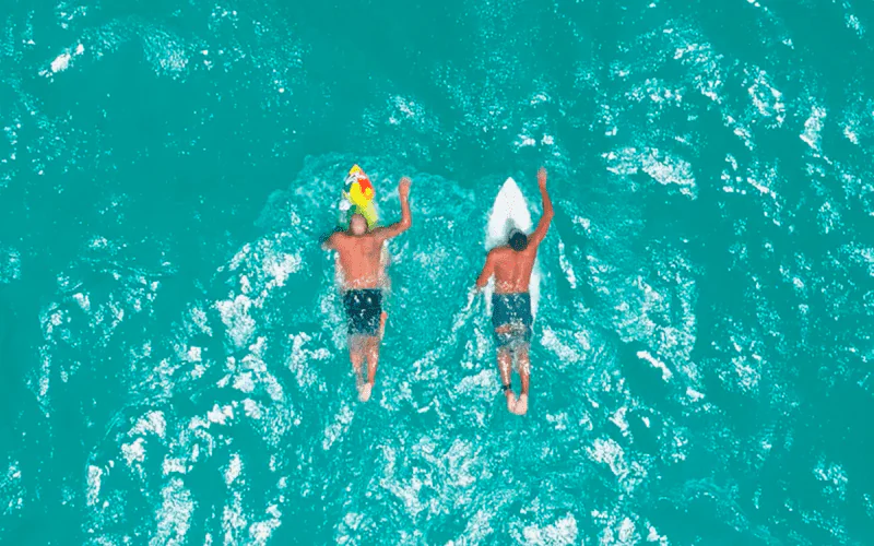 Duas pessoas deitadas em uma prancha de surf no mar