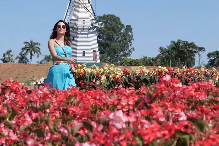 Uma mulher cercada de flores, na frente de um moinho
