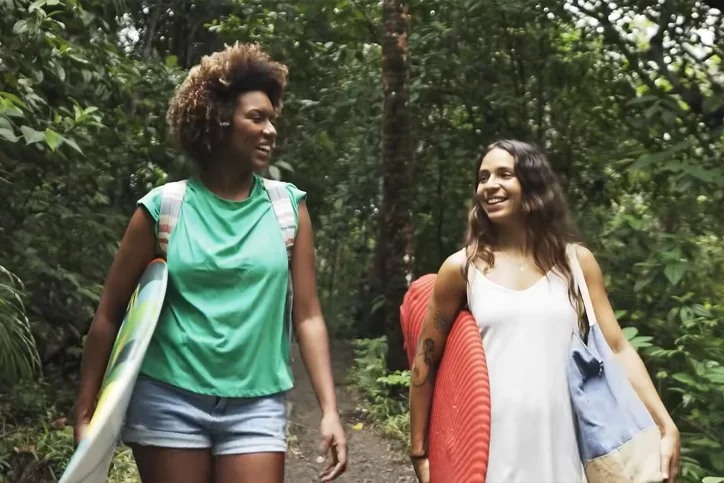 Duas mulheres se olhando e rindo, com pranchas na mão