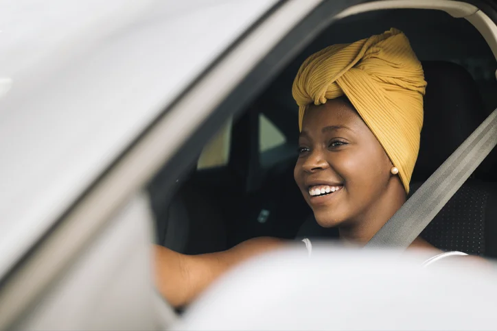 Mulher sorrindo com o carro parado e a cabeça encostada no volante.