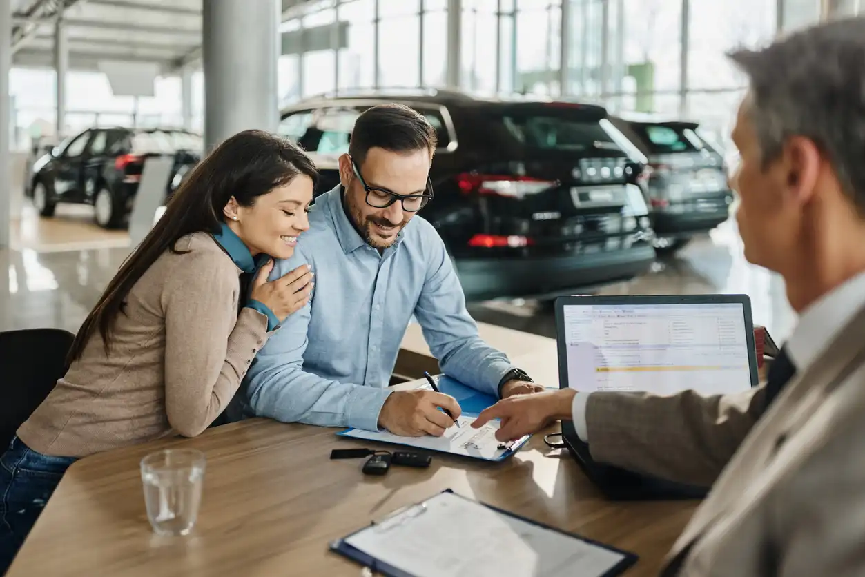 Como escolher um carro por assinatura: passo a passo e melhor opção Casal satisfeito realizando a compra de um carro em uma concessionária, com atendimento personalizado de um vendedor, destacando a experiência de compra e a confiança na aquisição de veículos.