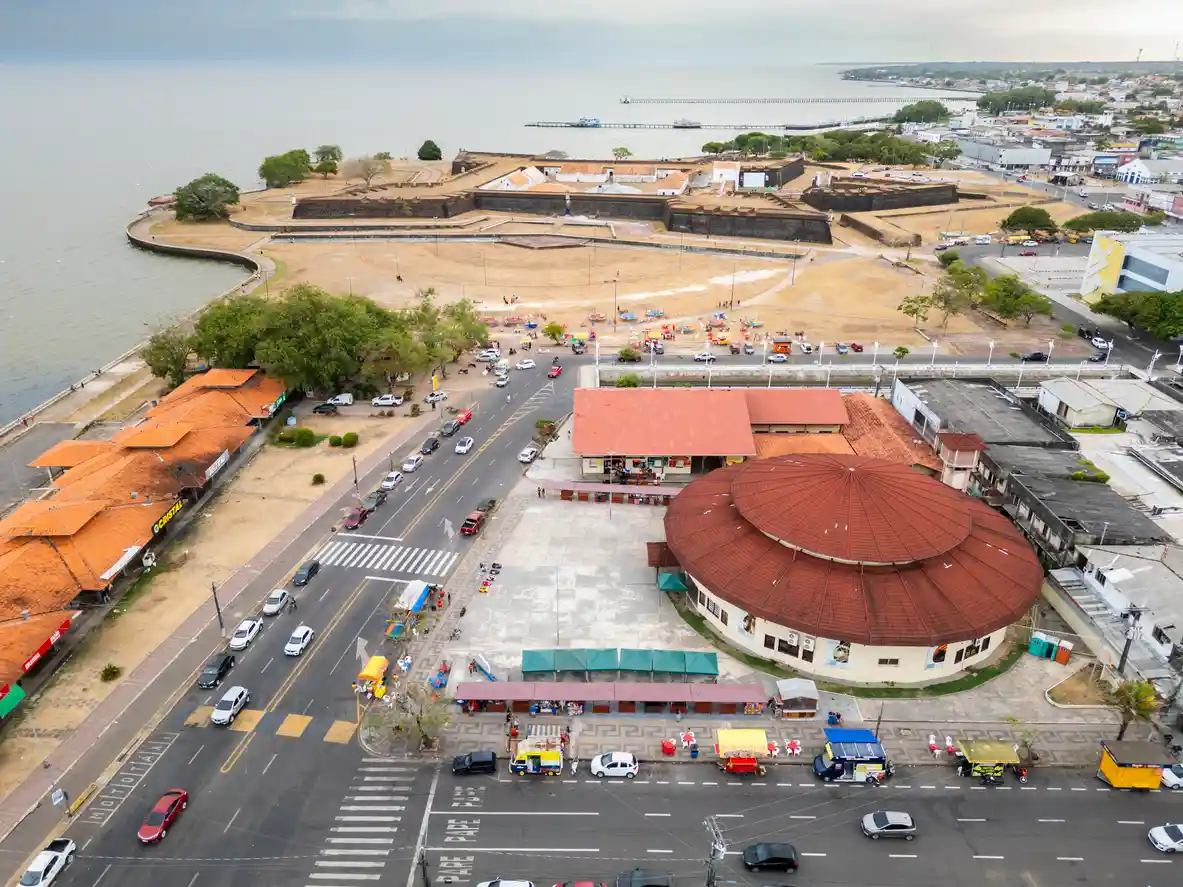 Vista aérea dos destinos turísticos da cidade de Macapá, destacando praias, áreas comerciais e pontos históricos na orla do rio Amazonas, em uma manhã ensolarada.